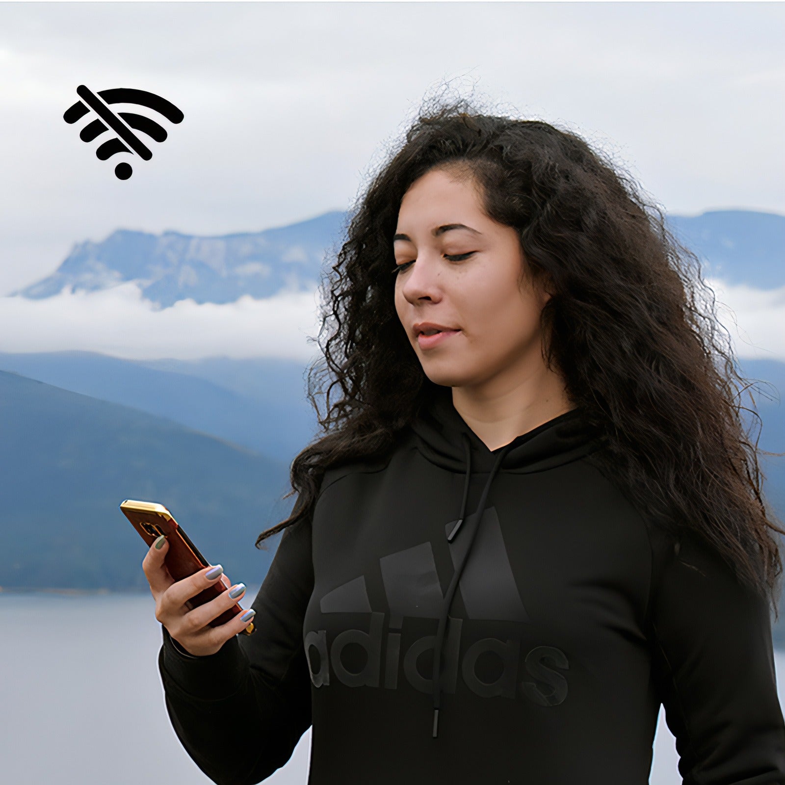 Femme portant un sweat à capuche noir Adidas utilisant un téléphone avec des montagnes en arrière-plan